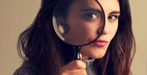 Studio portrait of a young woman looking through a magnifying glass against a brown background